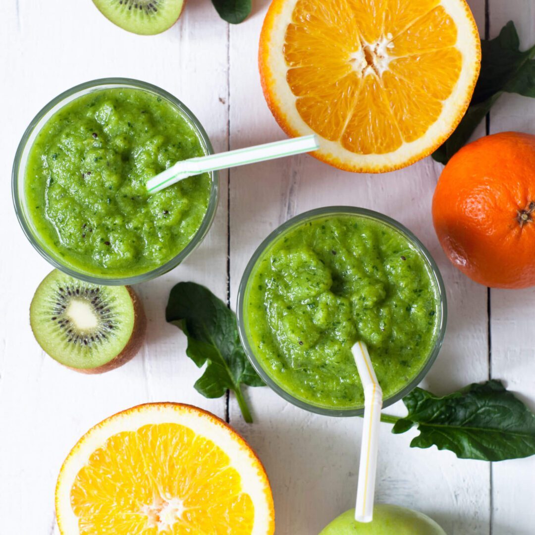 A table topped with green smoothies and fruit.